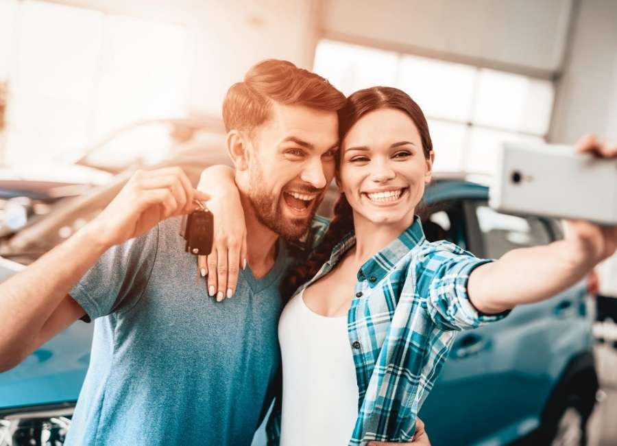 Couple taking a selfie in front of their new car