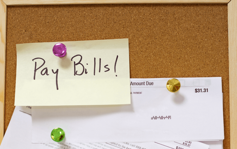 "Pay Bills!" sticky note on a bulletin board