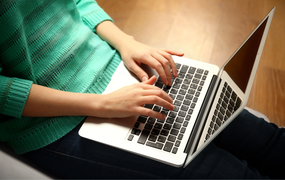 Person in teal sweater typing on laptop