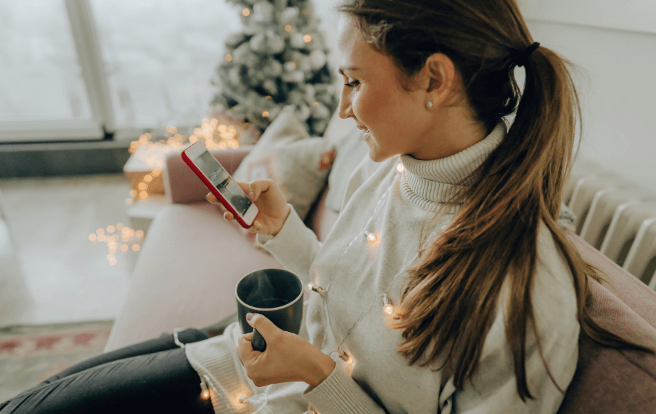woman looking at her phone while drinking coffee on the couch