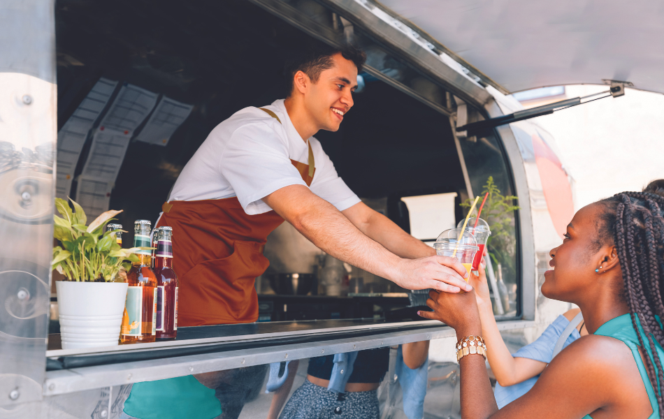 Man working in a food truck handing order to woman