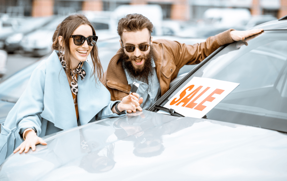 Two people next to a car that has a "sale" sign on it