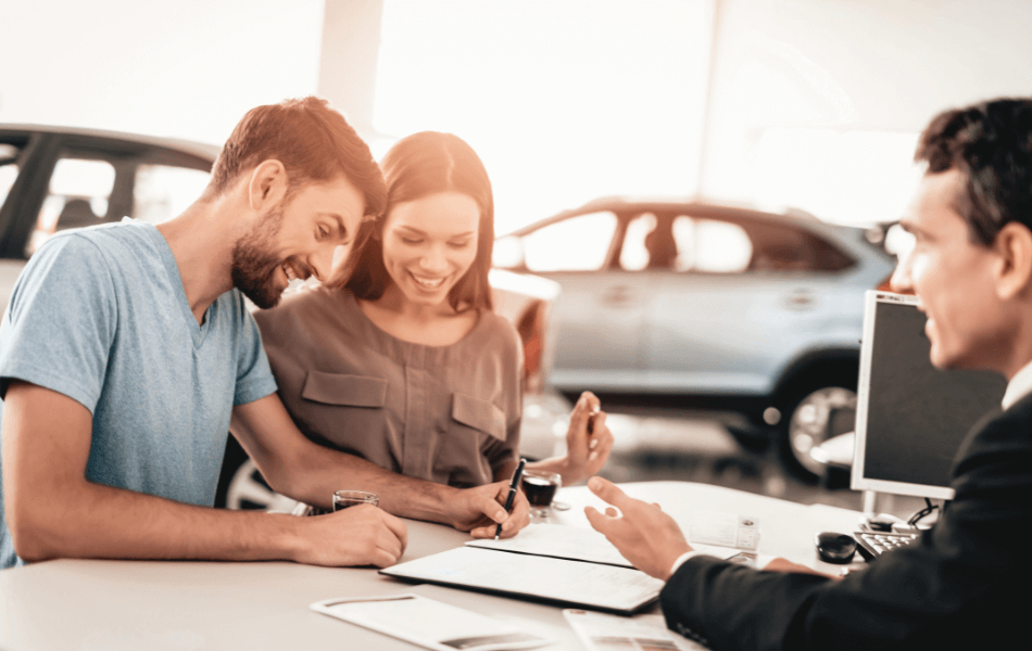 A couple signing papers at a car dealership