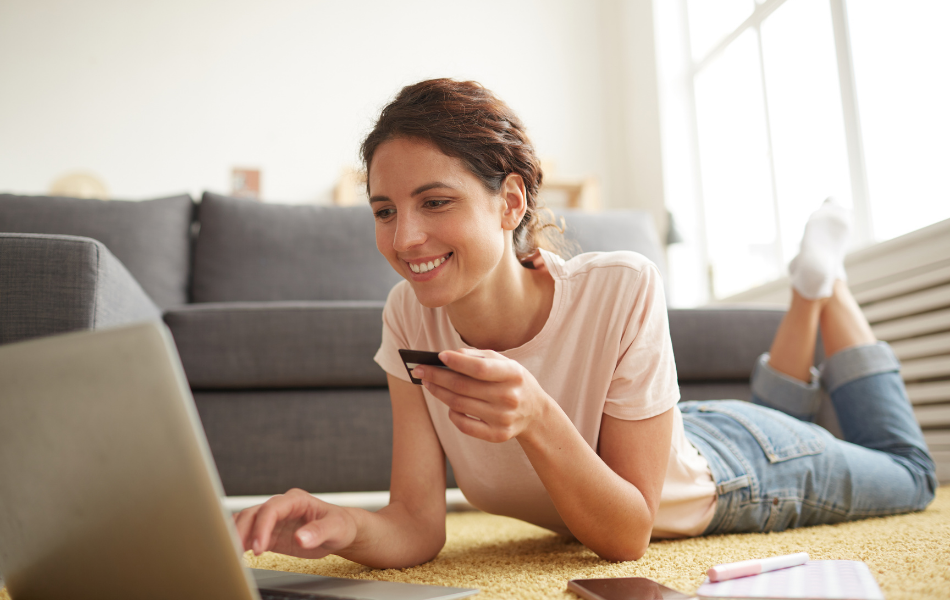 Avoid Gift Card Scams - Woman laying on floor purchasing gift card on her laptop with her credit card