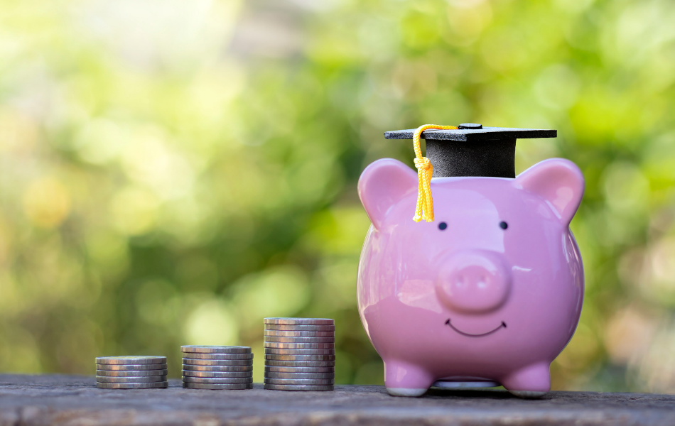 Financial Education - Pink piggy bank sitting next to a stack of coins wearing a graduation cap