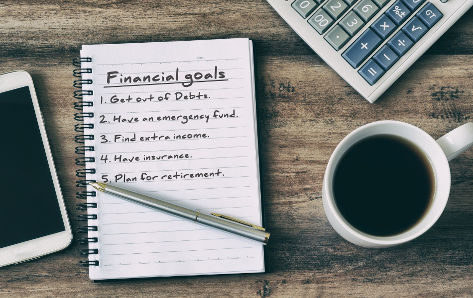 Set Financial Goals - An open notebook with writing, a cup of coffee, a cell phone and a calculator sit on a desk