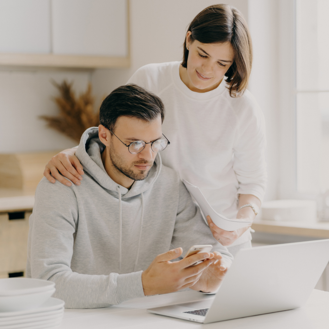 a man looking at a laptop and woman standing behind him